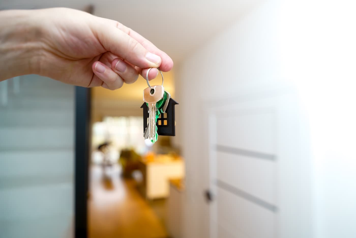 Hand mit Hausschlüssel vor einer Eingangstür – Symbol für den ersten Immobilienkauf